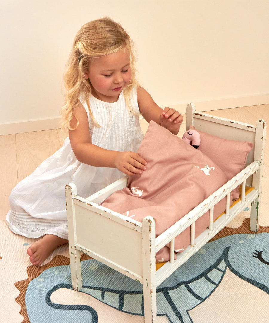 A child playing with a Roommate teddy inside a dolls bed, with the Roommate Doll Bedding Set - Rabbit