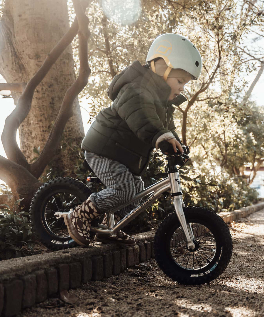 A child going down a raised brick boarder of a path, showing how robust the Early Rider Big Foot Balance Bikes are, and that they can be used on different terrains.