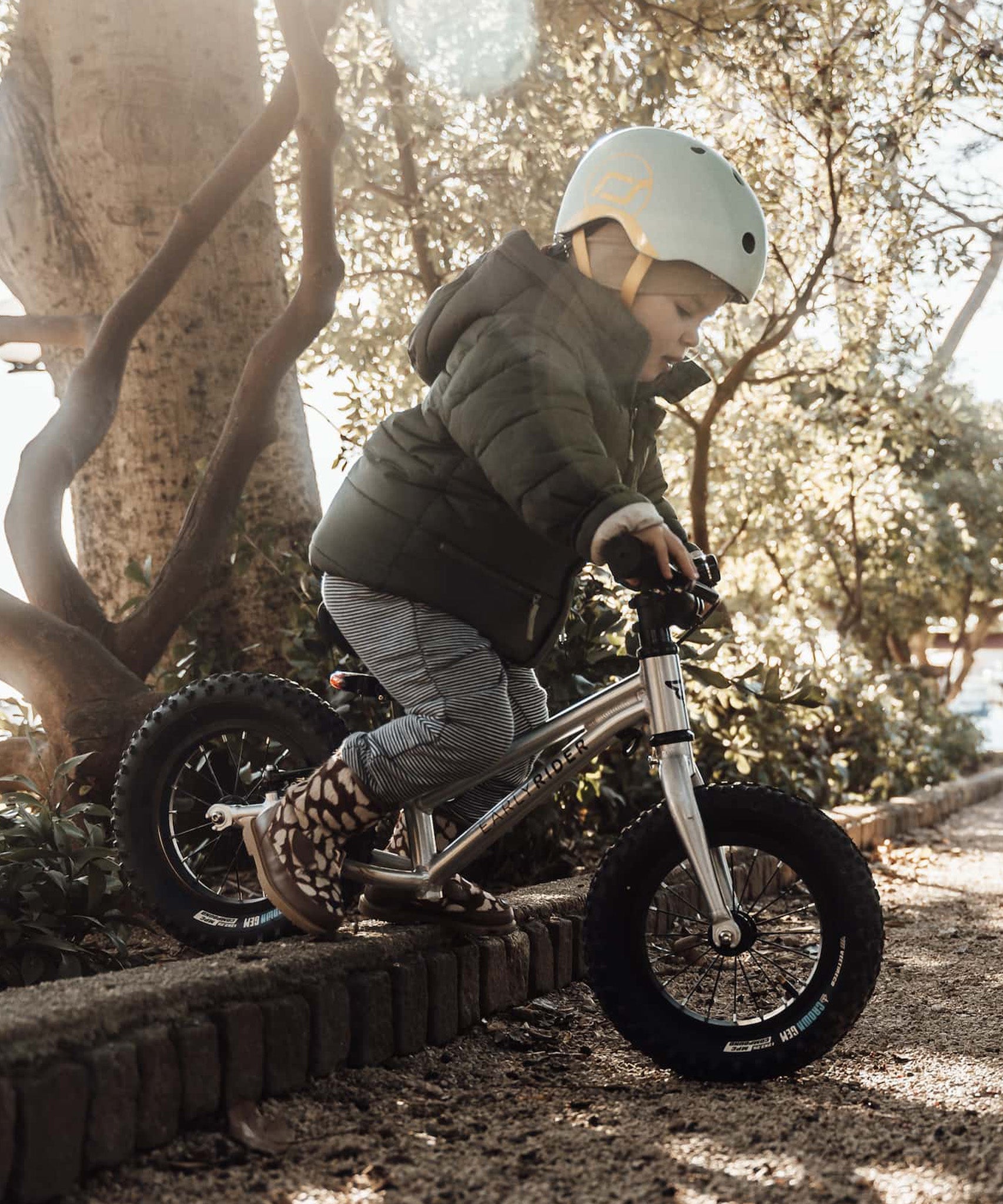 A child going down a raised brick boarder of a path, showing how robust the Early Rider Big Foot Balance Bikes are, and that they can be used on different terrains.