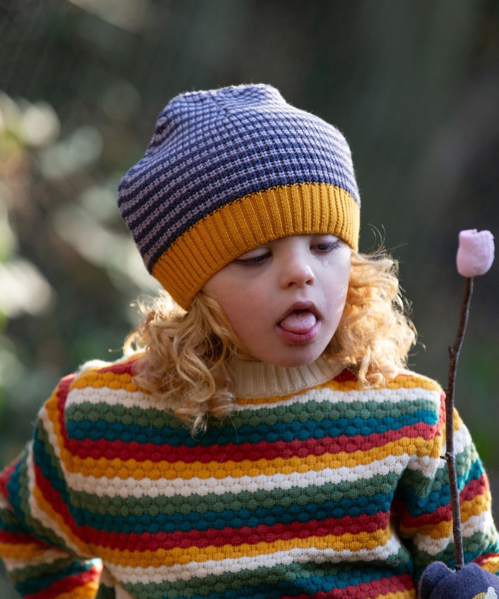 A child outside, holding a marshmallow on a stick, wearing the Dreamy Blue Knitted Beanie Hat