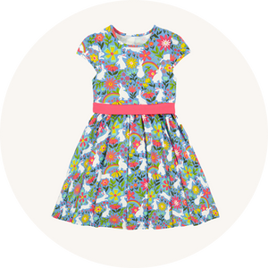 Frugi Issey Party Skater Dress Bunny Bounce - GOTS organic cotton with a busy print featuring flowers, rainbows and bunnies on a lavender background, a thick pink waistband and cap sleeves.