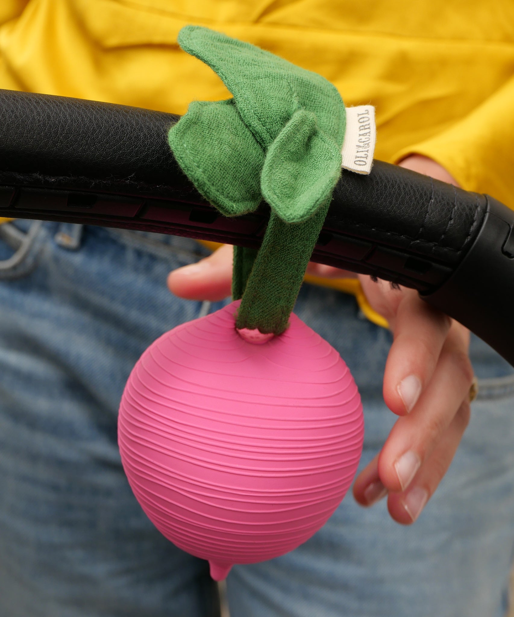 The texture of the Ramona Radish Pacifier Holder which has been tied onto a pram handle. A persons hand is reaching towards the holder.