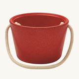 The side of the PlanToys red bucket, from the Sand Play set showing the beige rope handle, on a cream background