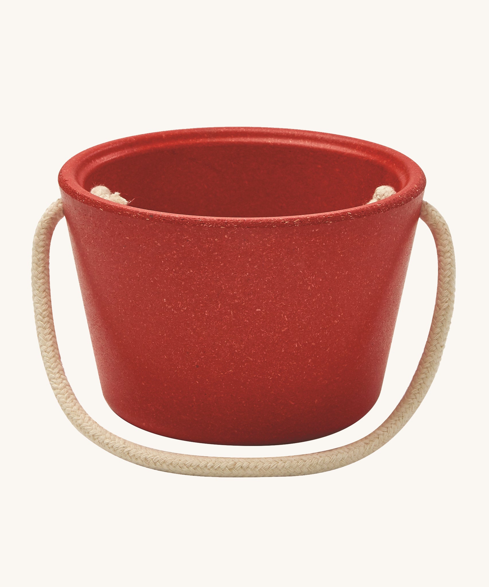 The side of the PlanToys red bucket, from the Sand Play set showing the beige rope handle, on a cream background