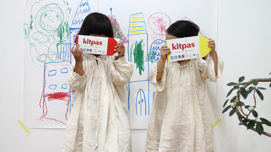 Two children holding up Kitpas drawing kids, standing in front of their drawing