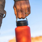 A person holding a Klean Kanteen bottle with the Klean Kanteen Wide Loop Cap - With Bale, by the carry handle