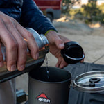 A person holding the Klean Kanteen Wide Loop Cap - With Bale, in their hand whilst pouring a drink from a Klean Kanteen