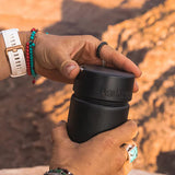 A person twisting the Klean Kanteen Wide Loop Cap - With Bale, in black, with a mountain background