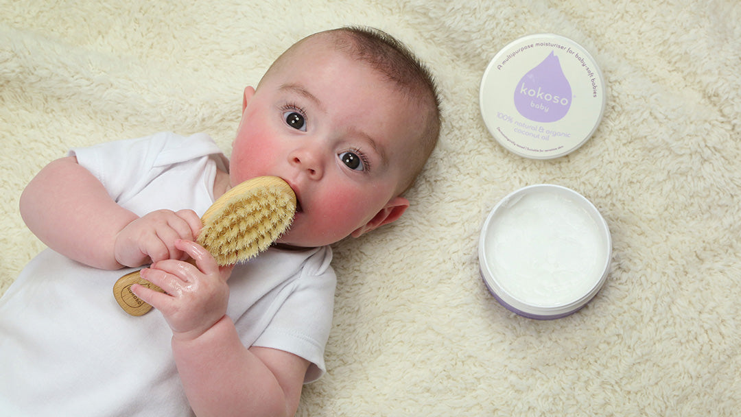 Baby holding a hairbrush, next to Kokoso coconut oil skincare products