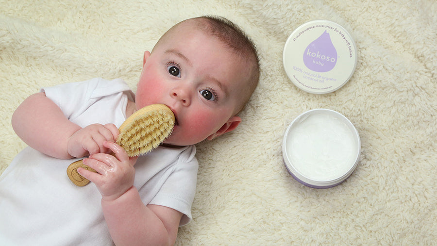 Baby holding a hairbrush, next to Kokoso coconut oil skincare products