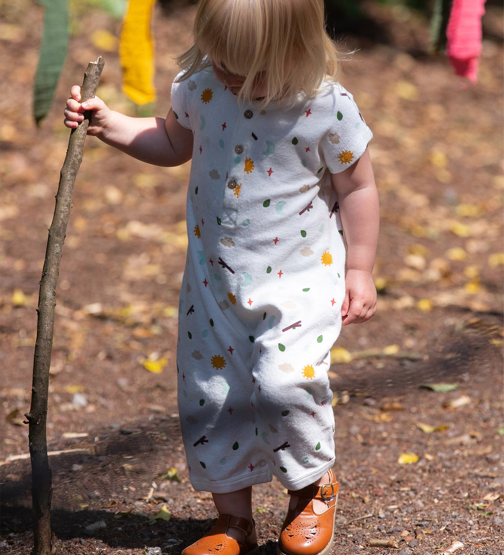 A child playing outside with a stick, wearing the LGR Adventure Baby Towelling Romper