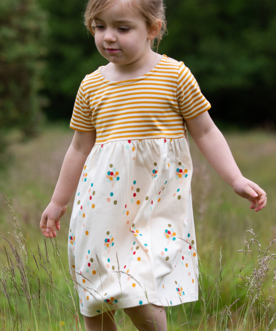 A child playing in a grassy field wearing the LGR Rainbow Balloons Easy Peasy Summer Dress