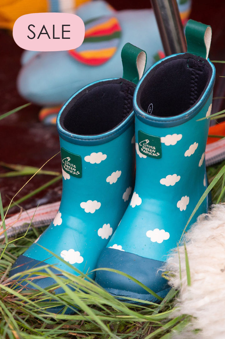 A pair of blue rubber wellingtons from Little Green Radicals on a grass floor to represent Little Green Radicals sale at Babipur.