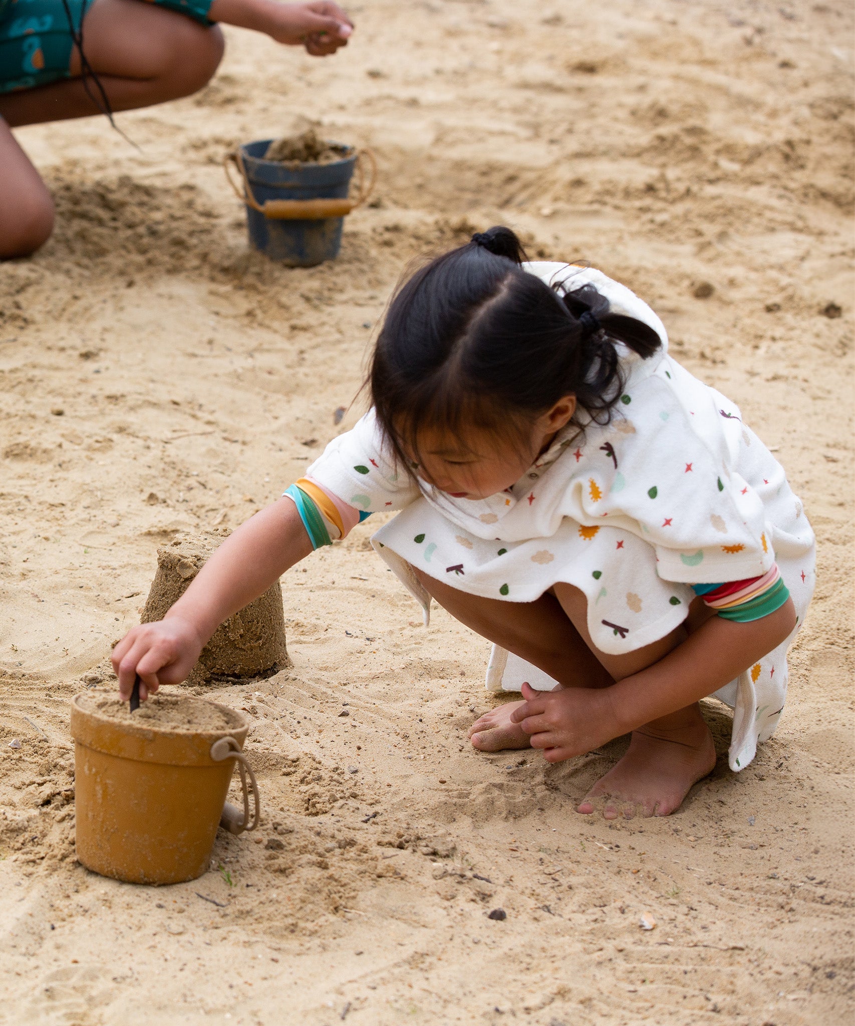 A child making sand castles, whilst wearing the LGR Adventure Hooded Beach Towel Poncho