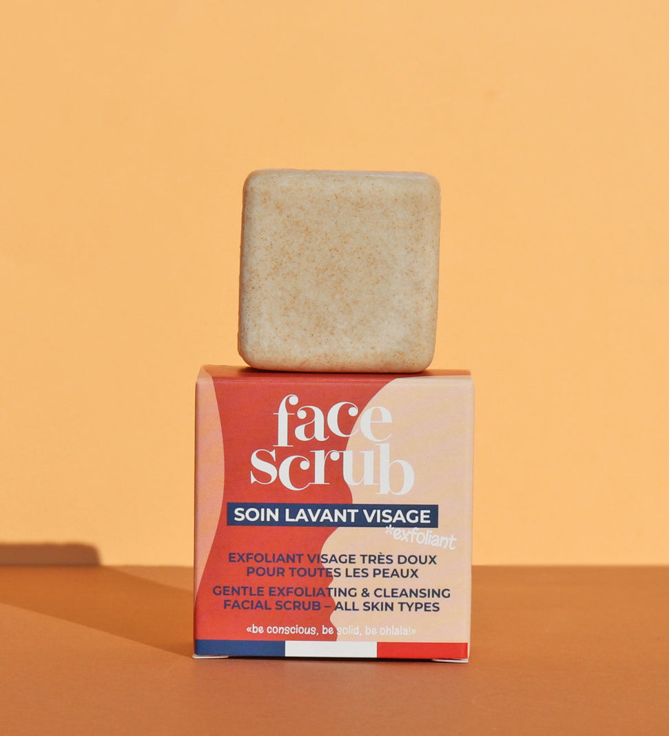 The Lamazuna Solid Face Scrub Bar stood on top of its packaging box, on a yellow and orange background