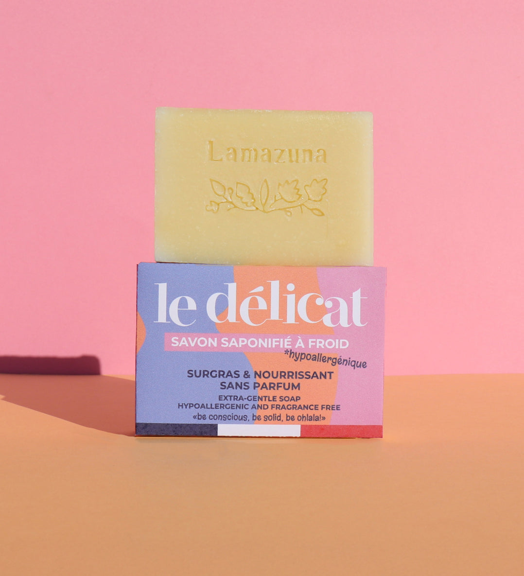 Lamazuna Sensitive Skin Soap Bar, on top of its packaging box, on a pink and orange background