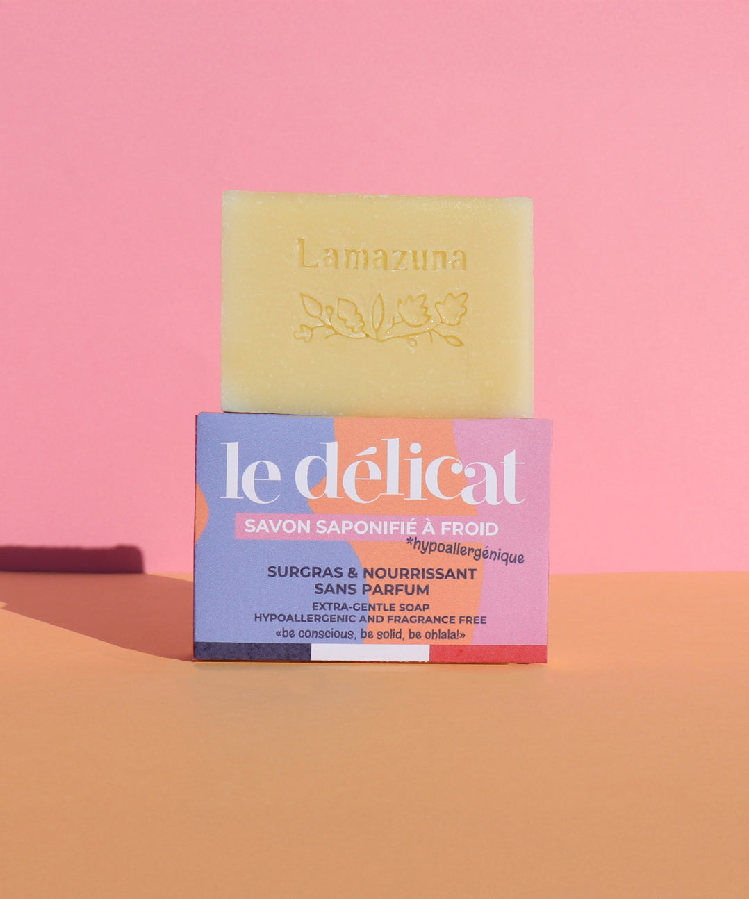 Lamazuna Sensitive Skin Soap Bar, on top of its packaging box, on a pink and orange background