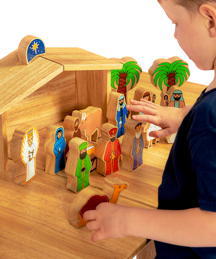 A child playing with the Lanka Kade Deluxe Nativity Set wooden figures on a wooden table