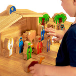 A child playing with the Lanka Kade Deluxe Nativity Set wooden figures on a wooden table