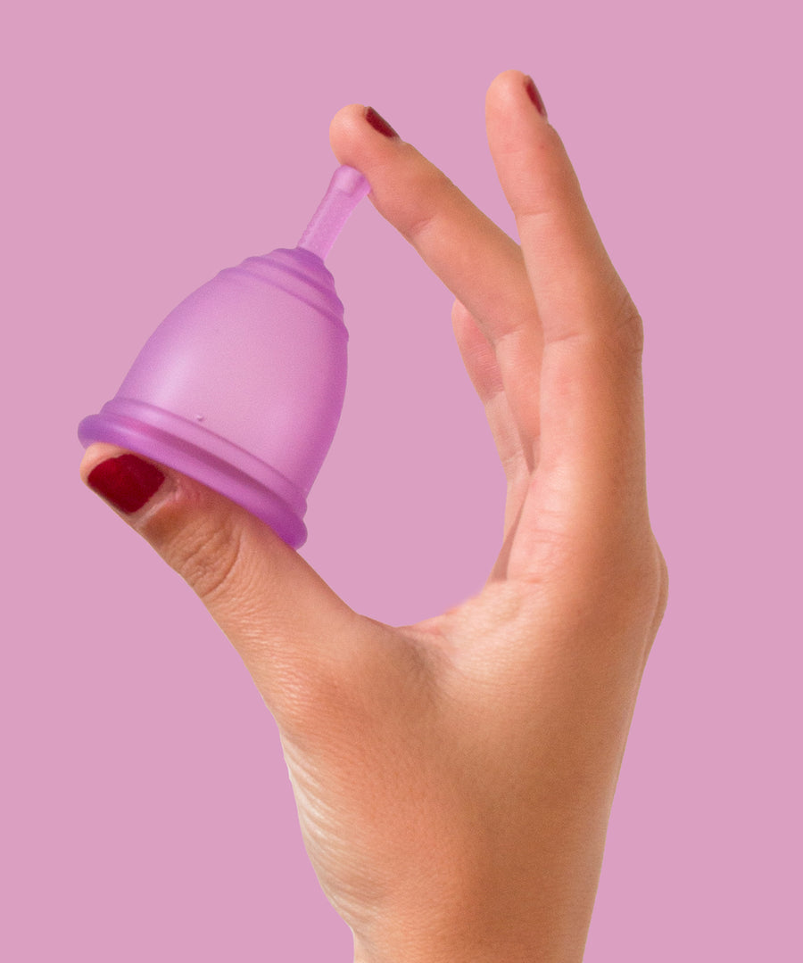 A person holding the Purple Silicone, BPA free and latex free Ruby Cup in between their fingers on a pink/purple background.