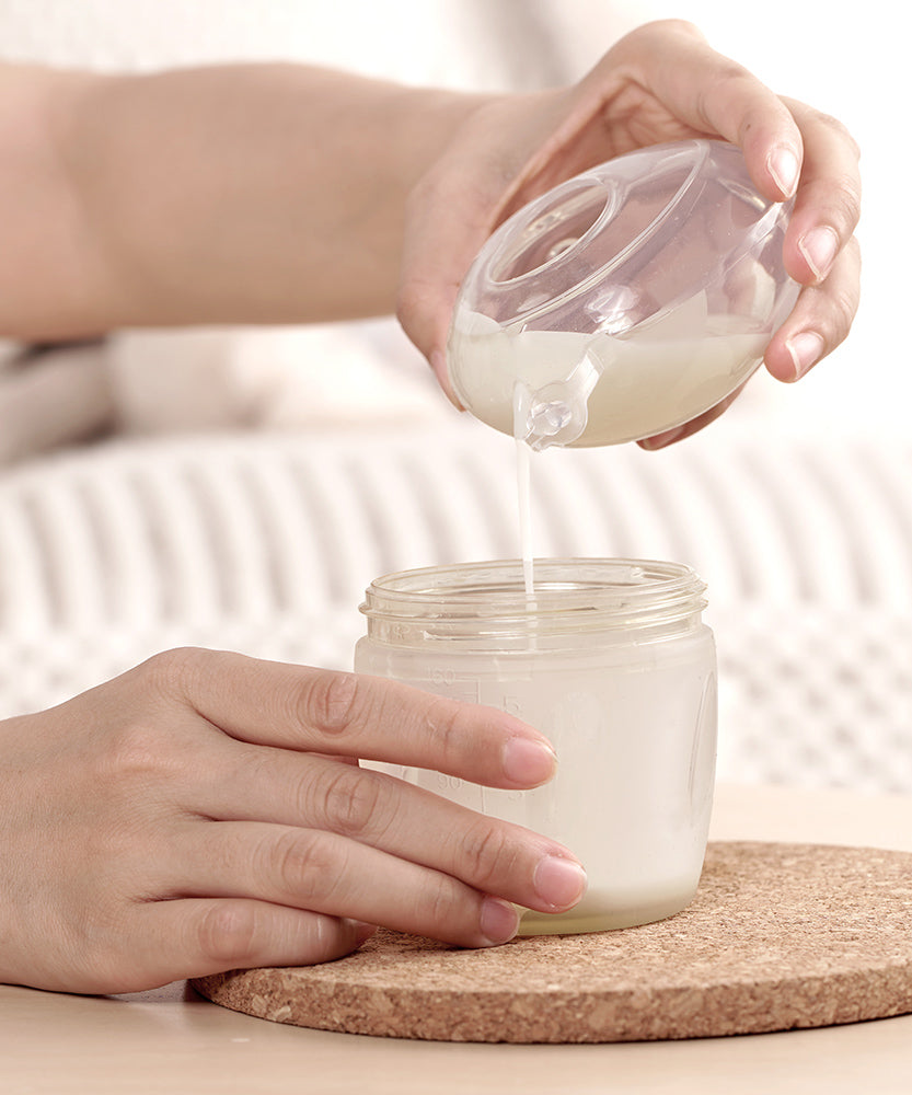 A person pouring milk from the Haakaa Ladybug Silicone Breast Milk Collector, into a Haakaa baby bottle