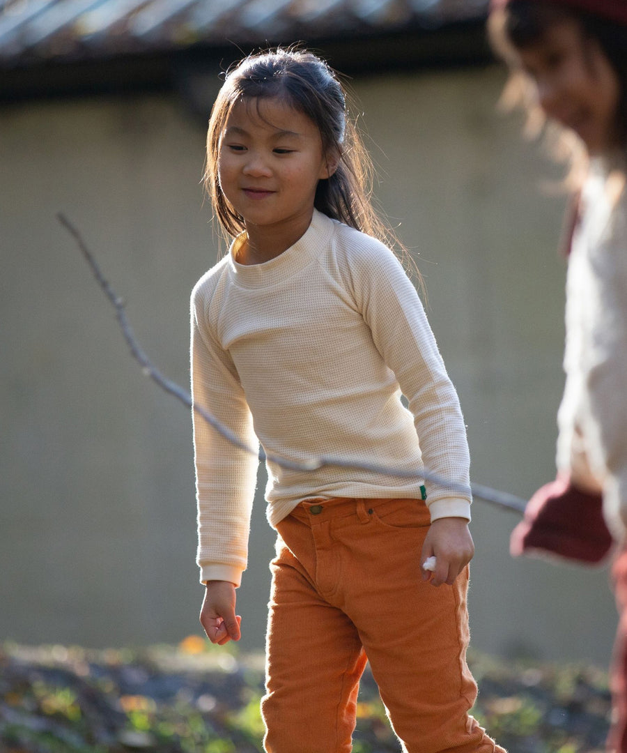 Children playing together outside and smiling. The child at the back of the image is wearing the  Little Green Radicals Long Sleeve Waffle Top - Cream