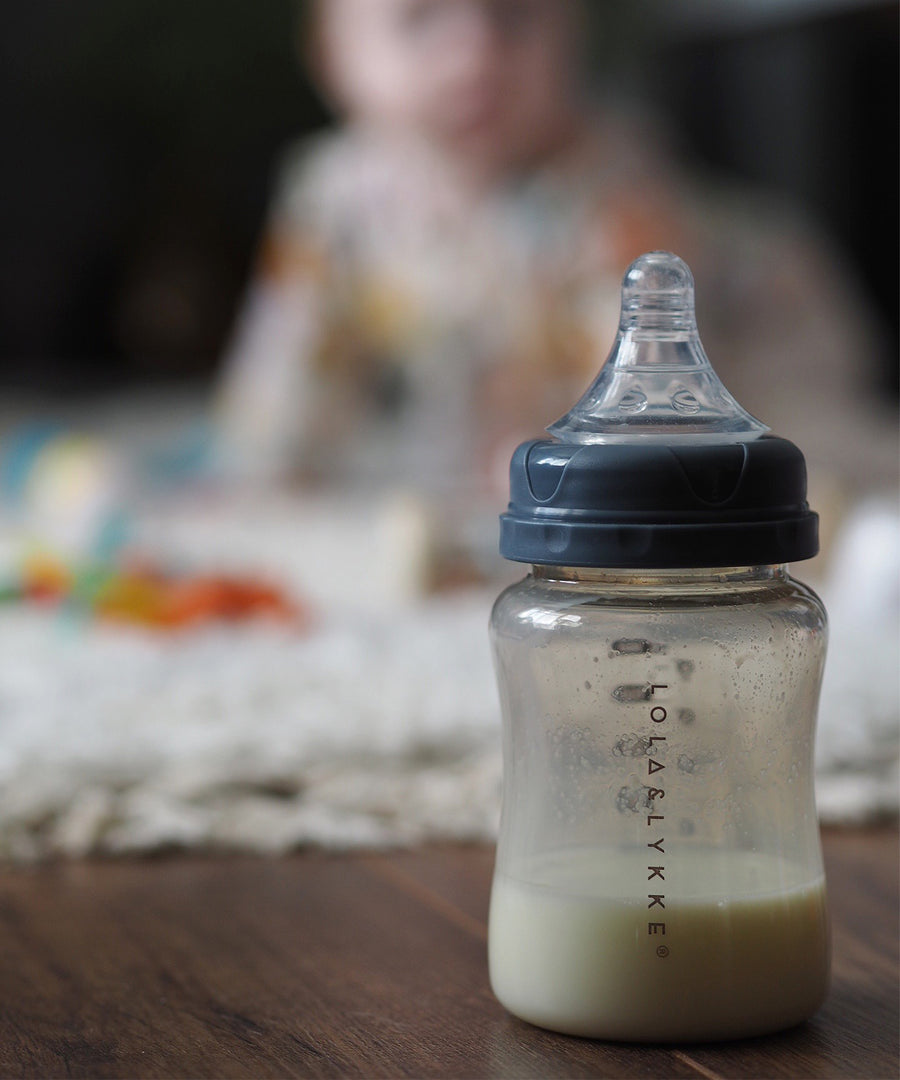 A Lola & Lykke bottle, with the Nipple Teat attached. A baby is in the background but is blurred as the image focuses on the bottle