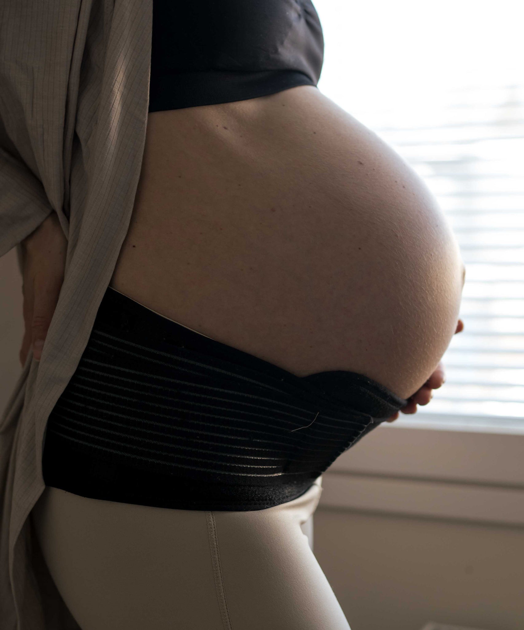 A person with their hand on their pregnancy bump, wearing the Lola & Lykke Core Relief Pregnancy Support Belt