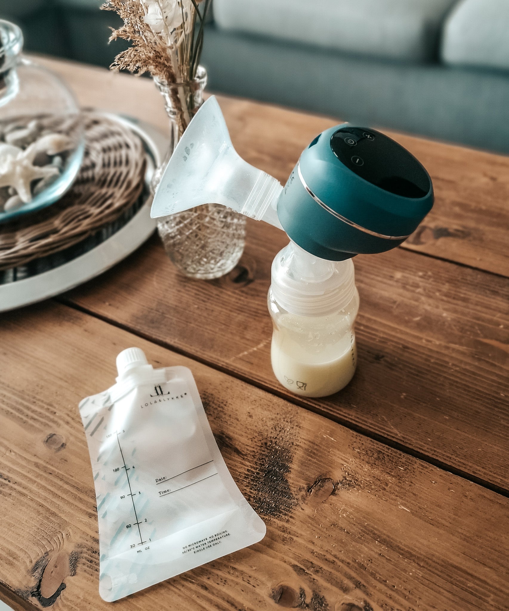 The Lola&Lykke Smart Electric Breast Pump and milk bag next to the pump. Both items are set on a wooden table