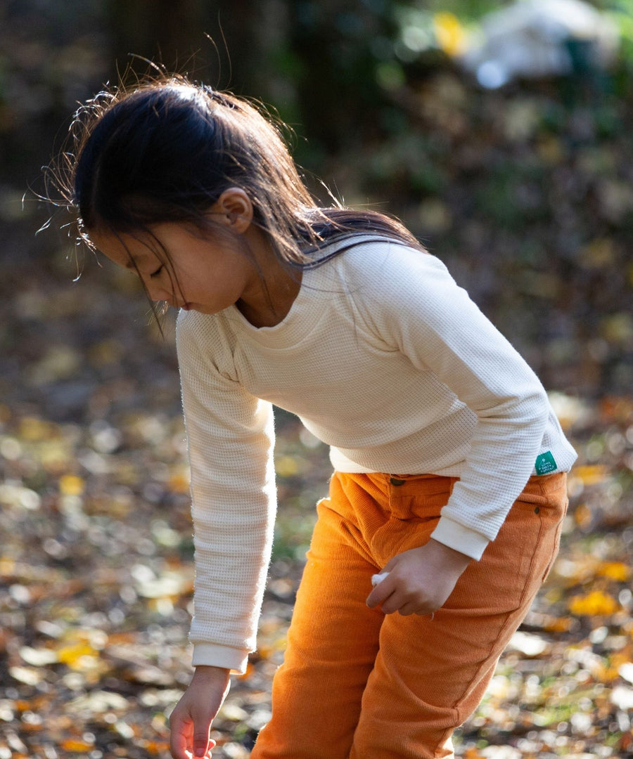 A child outside in the sun, playing  and wearing the Little Green Radicals Long Sleeve Waffle Top - Cream. They are also wearing yellow trousers