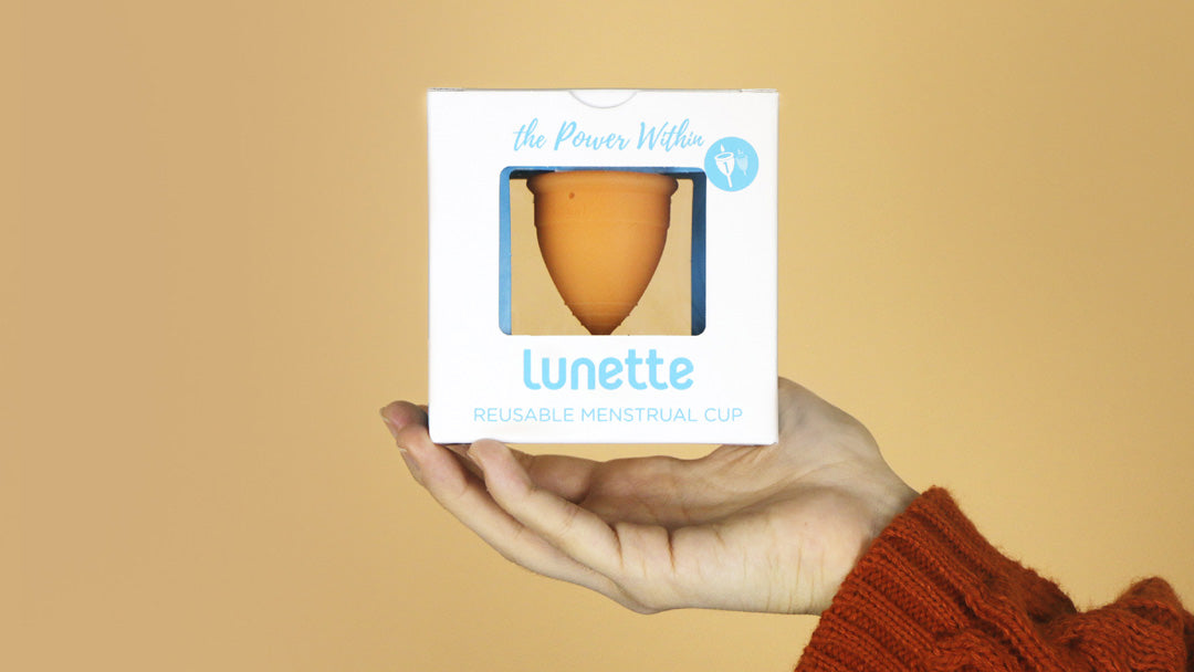 Hand holding up a Lunette menstrual cup in its box