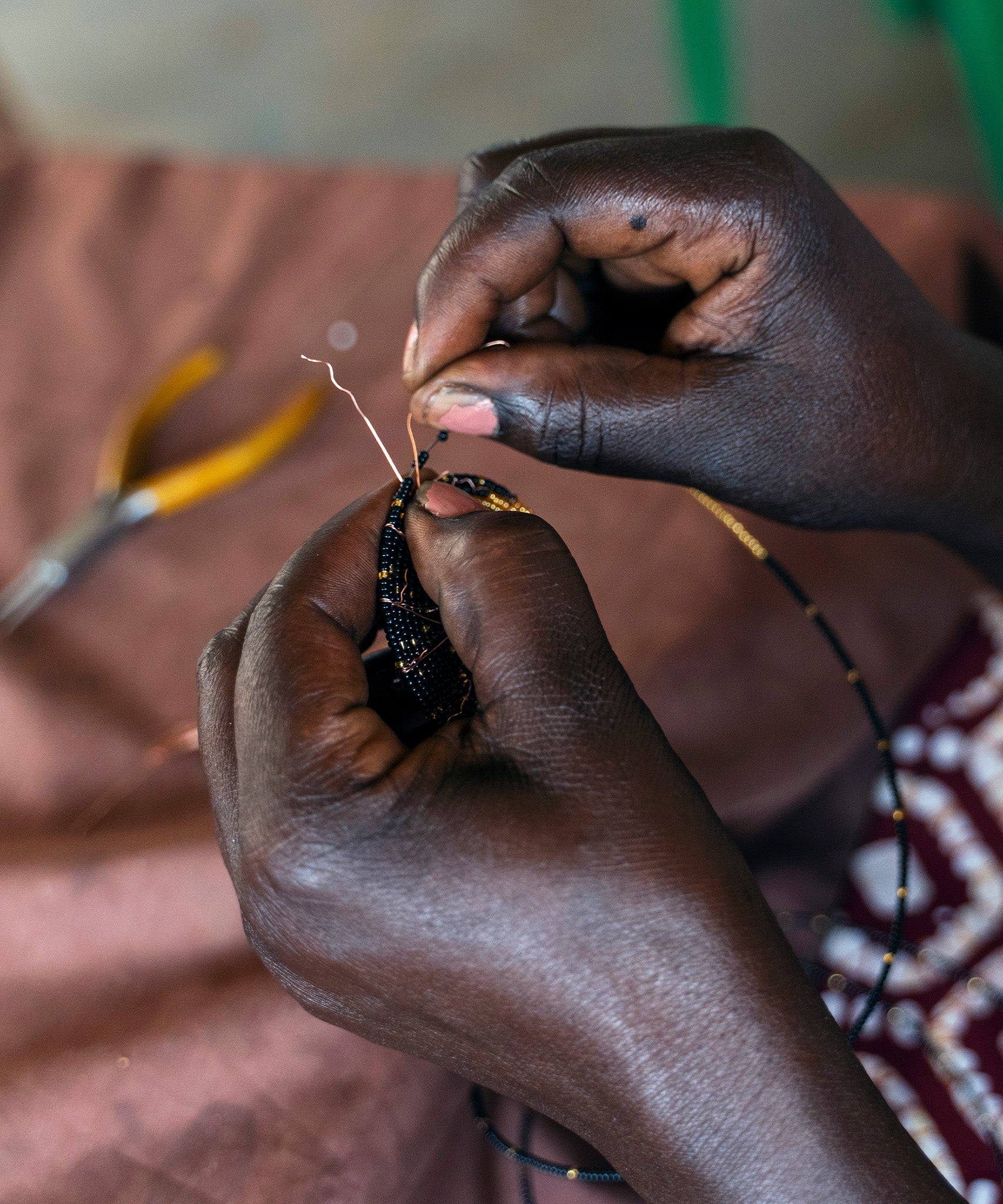 A look at the intricate hand making process. A person carefully threads gold and black glass beads onto copper wire