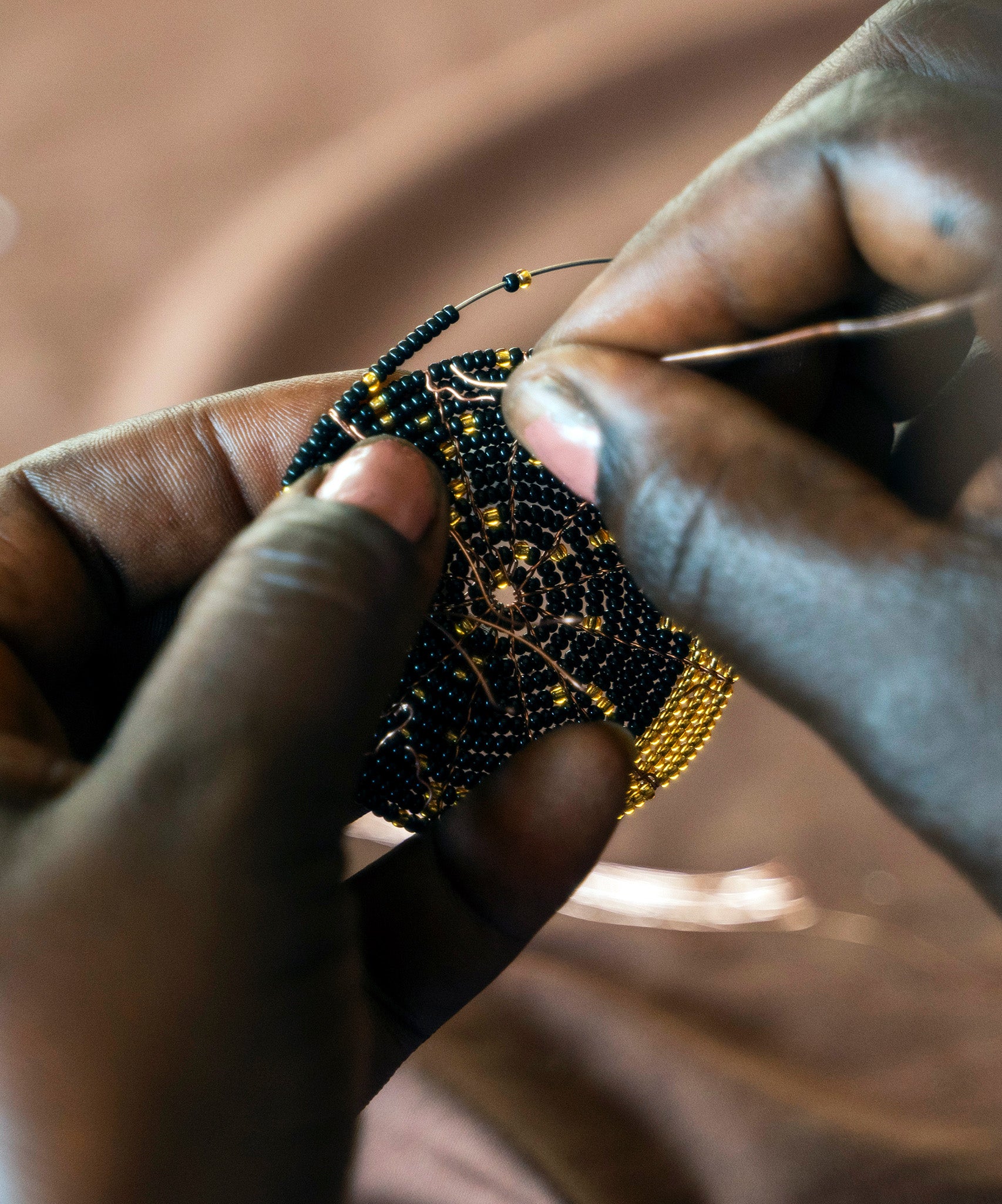 A look at the intricate hand making process. A person carefully threads gold and black glass beads onto copper wire