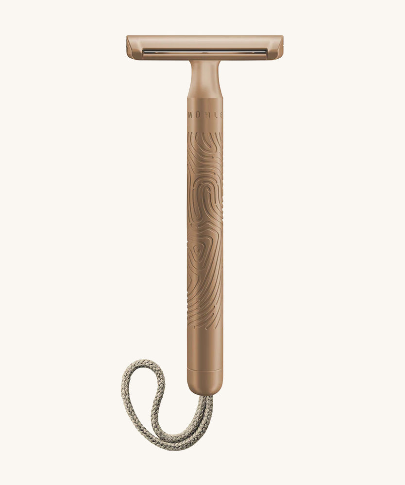 A rose gold Muhle steel safety razor with a natural cord on a cream background