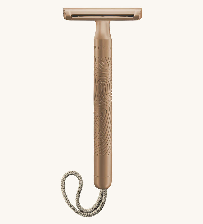 A rose gold Muhle steel safety razor with a natural cord on a cream background