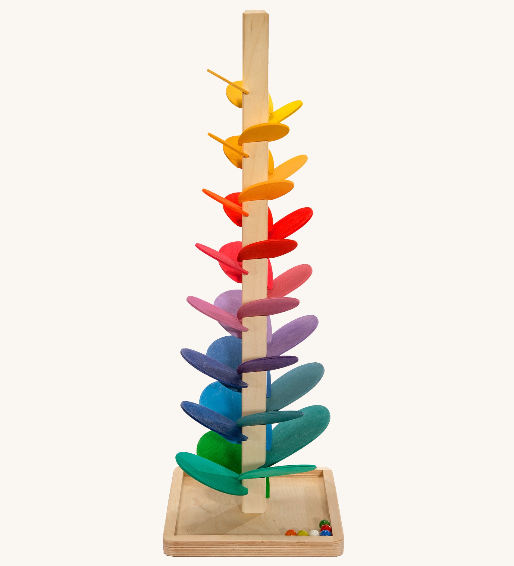 A large Magic Wood Marble Tree with colourful wooden leaves, stands with a light wooden stem on a light wooden base. There are 6 colourful marbles in the bottom right corner of the base. The Marble Tree is on a cream background