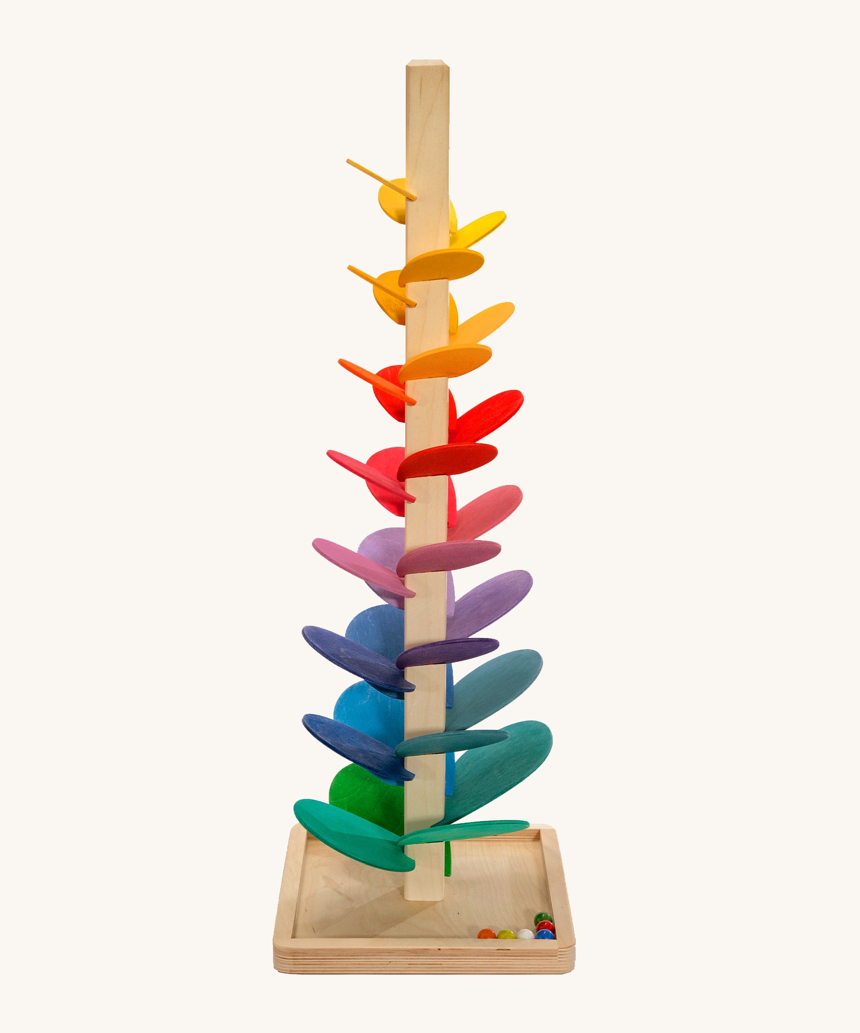 A large Magic Wood Marble Tree with colourful wooden leaves, stands with a light wooden stem on a light wooden base. There are 6 colourful marbles in the bottom right corner of the base. The Marble Tree is on a cream background