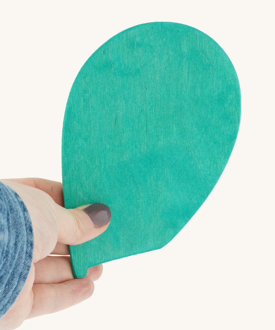 A person holding the Magic Wood Marble Tree Spare Leaf in their fingers. The leaf is made from wood and is a turquoise colour, on a cream background.