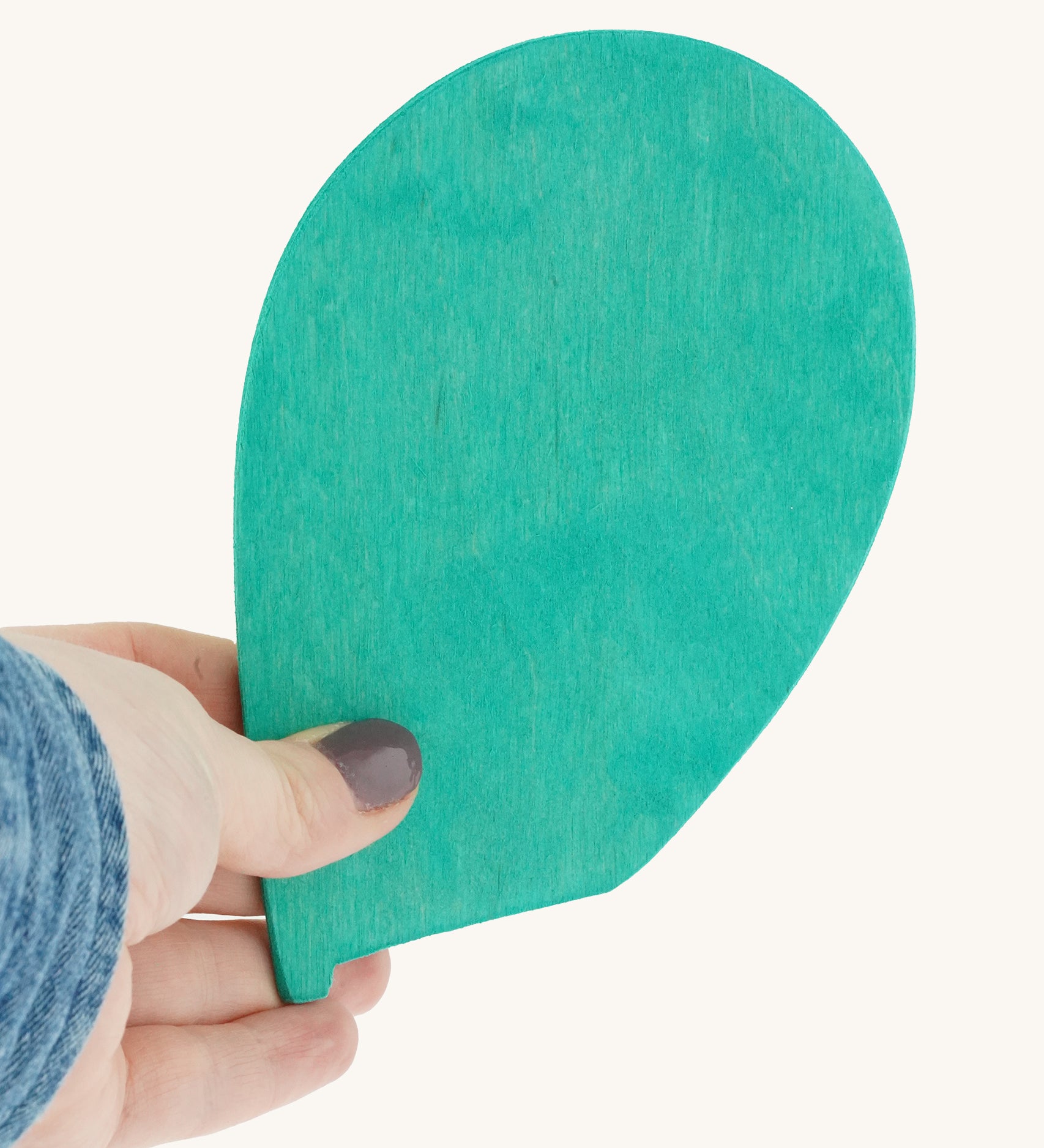 A person holding the Magic Wood Marble Tree Spare Leaf in their fingers. The leaf is made from wood and is a turquoise colour, on a cream background.