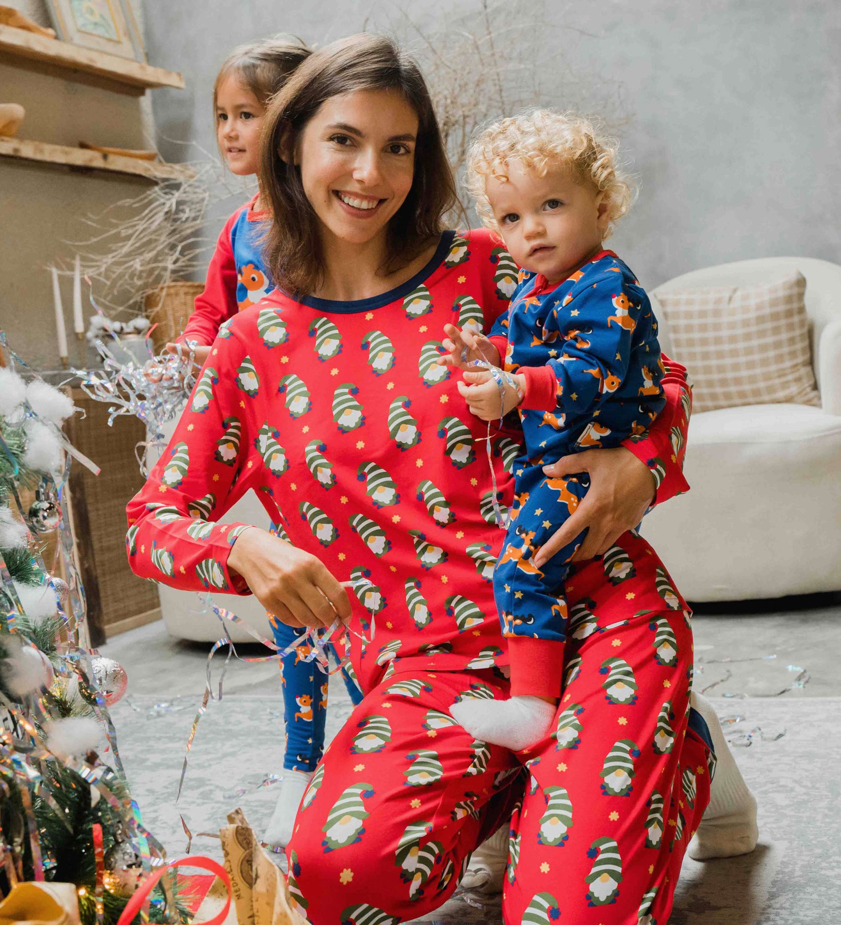 A woman wearing a Maxomorra Swedish Santa Adult Long Sleeve Pyjama Set holding a small child that is wearing a reindeer print rompersuit. 