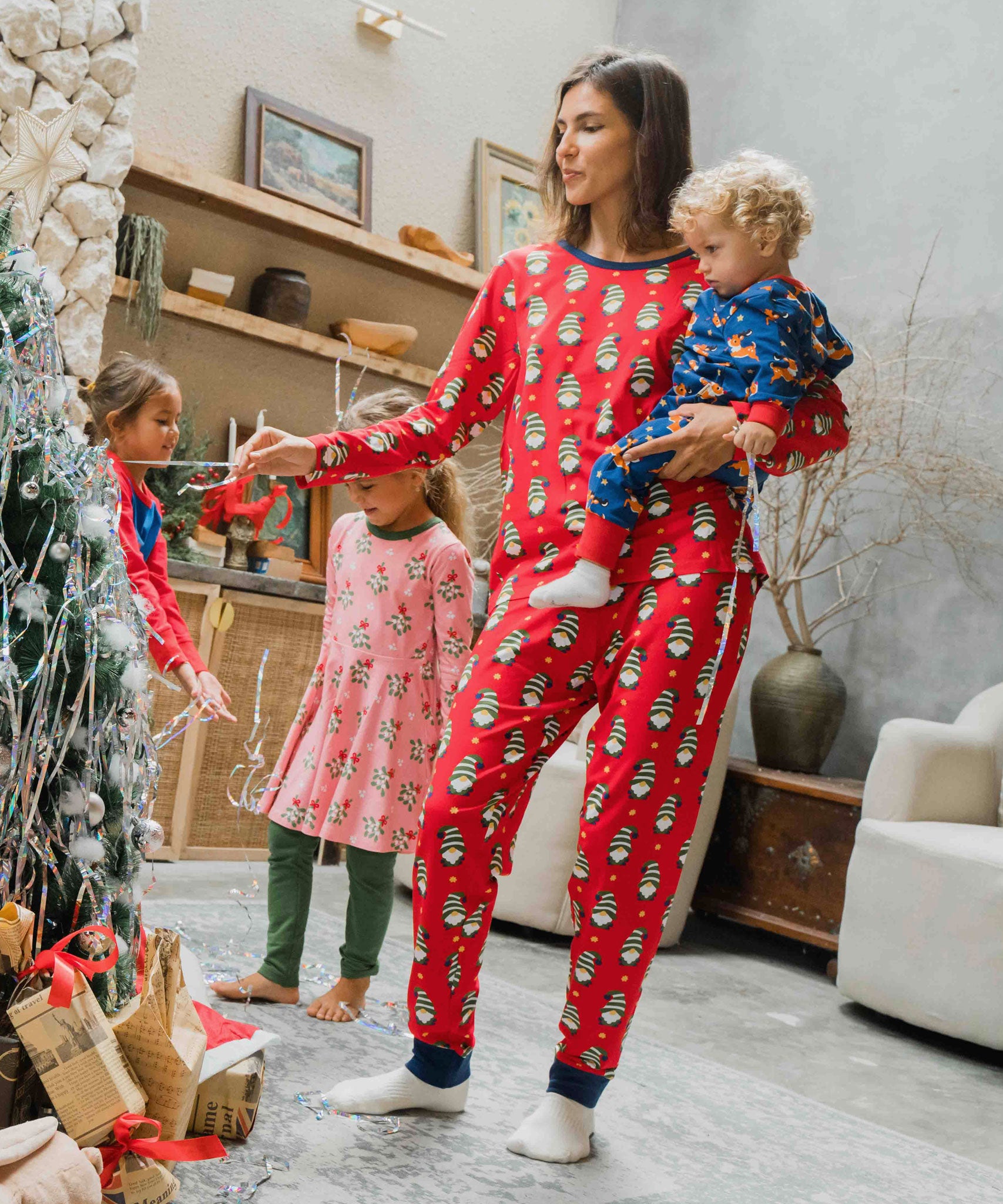 A woman wearing a Maxomorra Swedish Santa Adult Long Sleeve Pyjama Set holding a small child that is wearing a reindeer print rompersuit. 