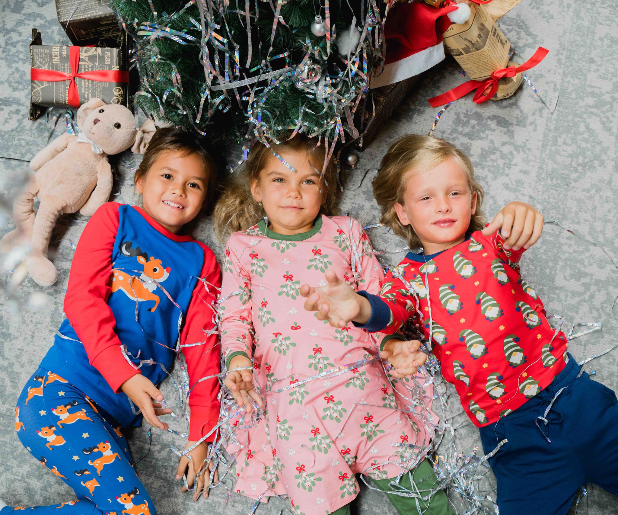 Three children lying on the floor looking up at the camera wearing clothing from the Maxomorra Christmas collection. 