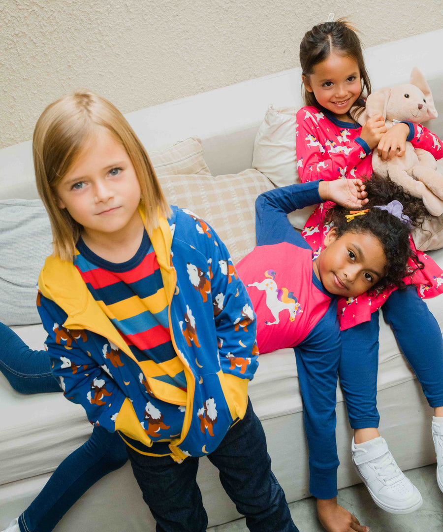 A child wearing a Maxomorra Wolf Reversible Zip Hoodie. Two other children can be seen in the background lying on a sofa.