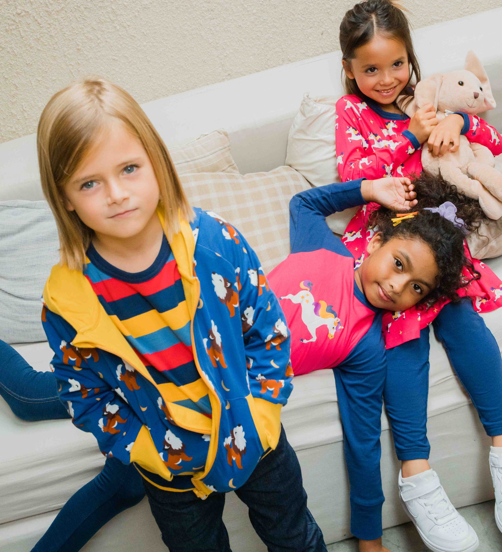 A child wearing a Maxomorra Wolf Reversible Zip Hoodie. Two other children can be seen in the background lying on a sofa.