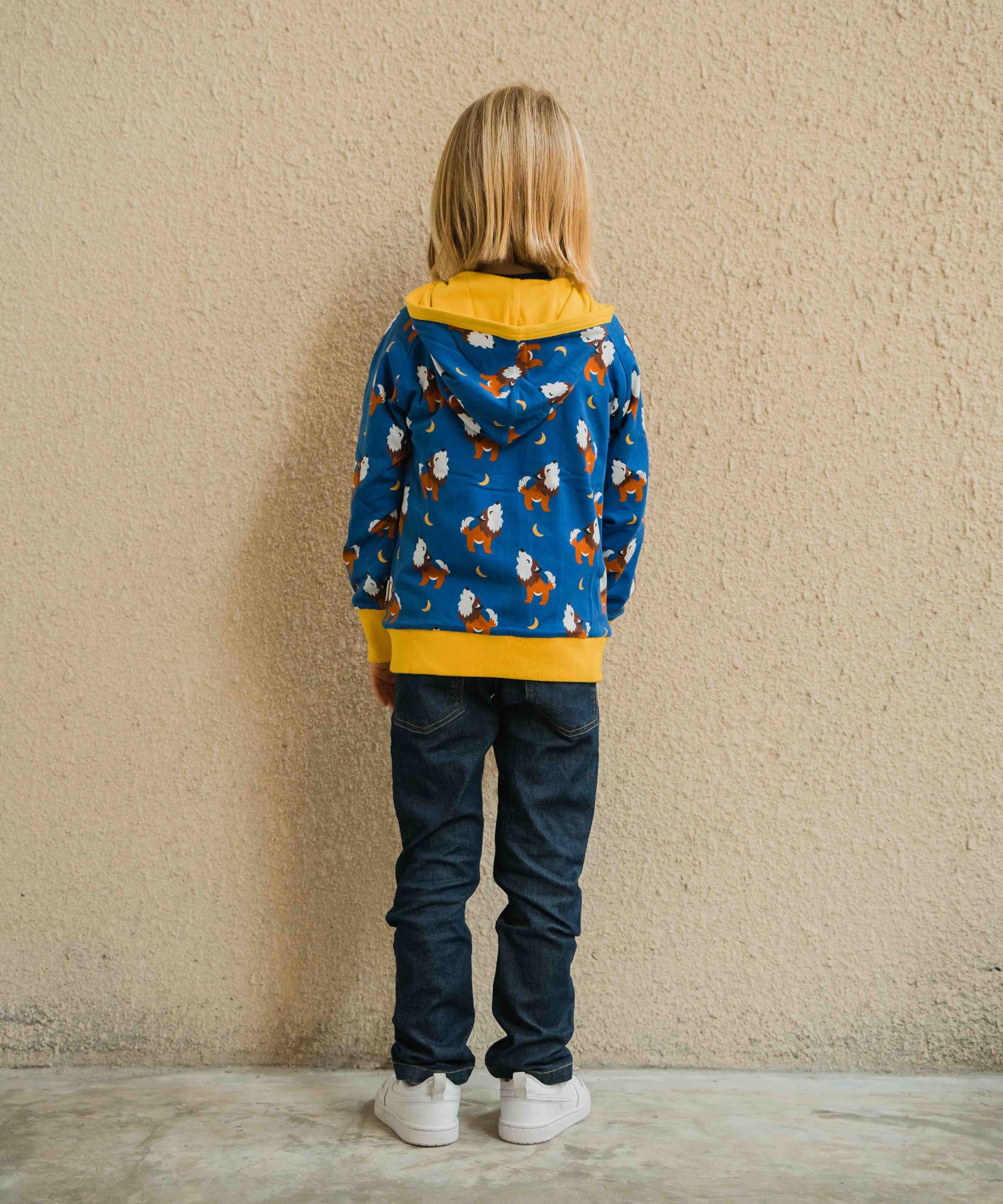 A child wearing a Maxomorra Wolf Reversible Zip Hoodie. The child is facing away from the camera showing the back of the hoodie. 