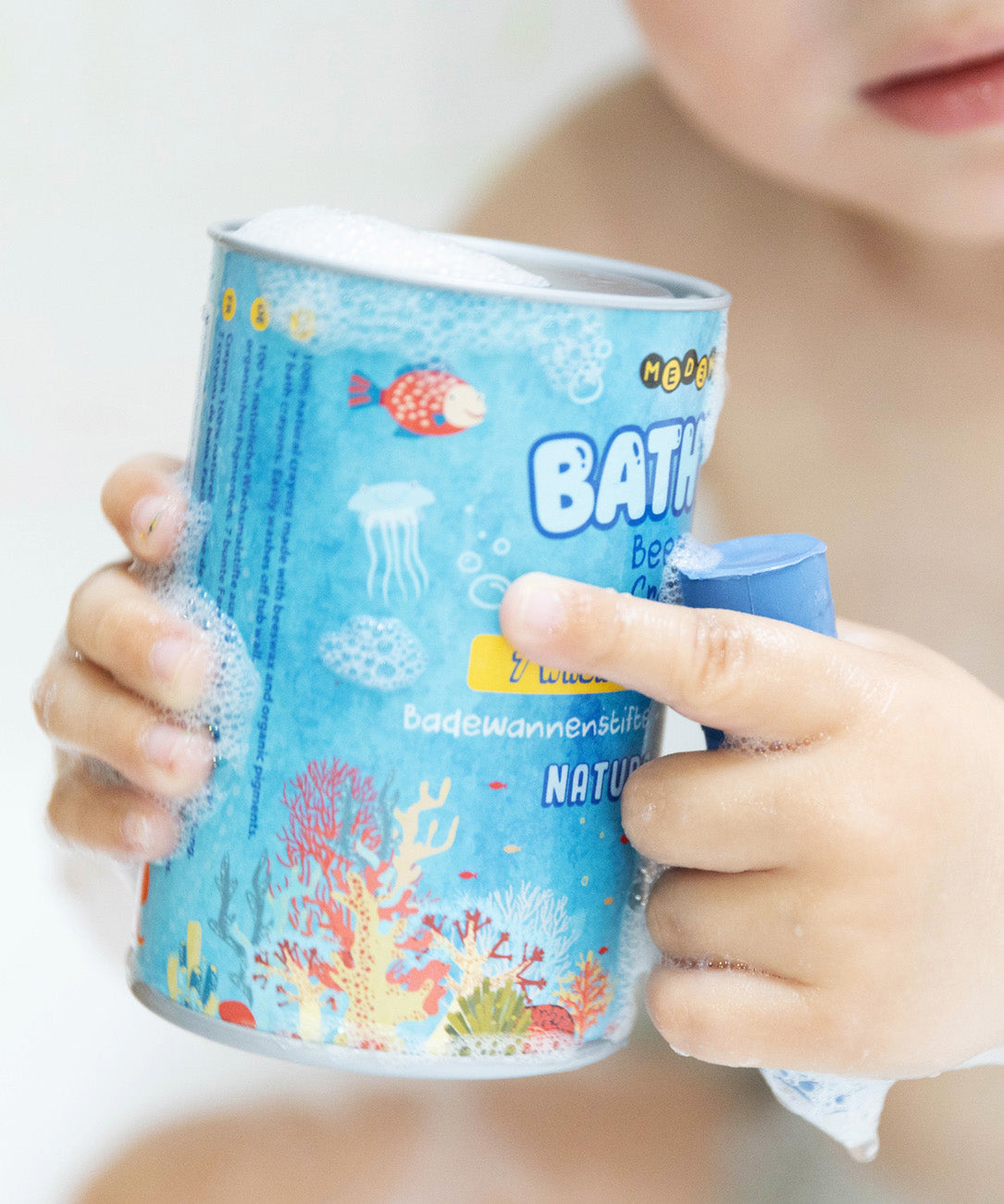 A baby holding a soapy box of Medenka beeswax bath crayons in the bath. 