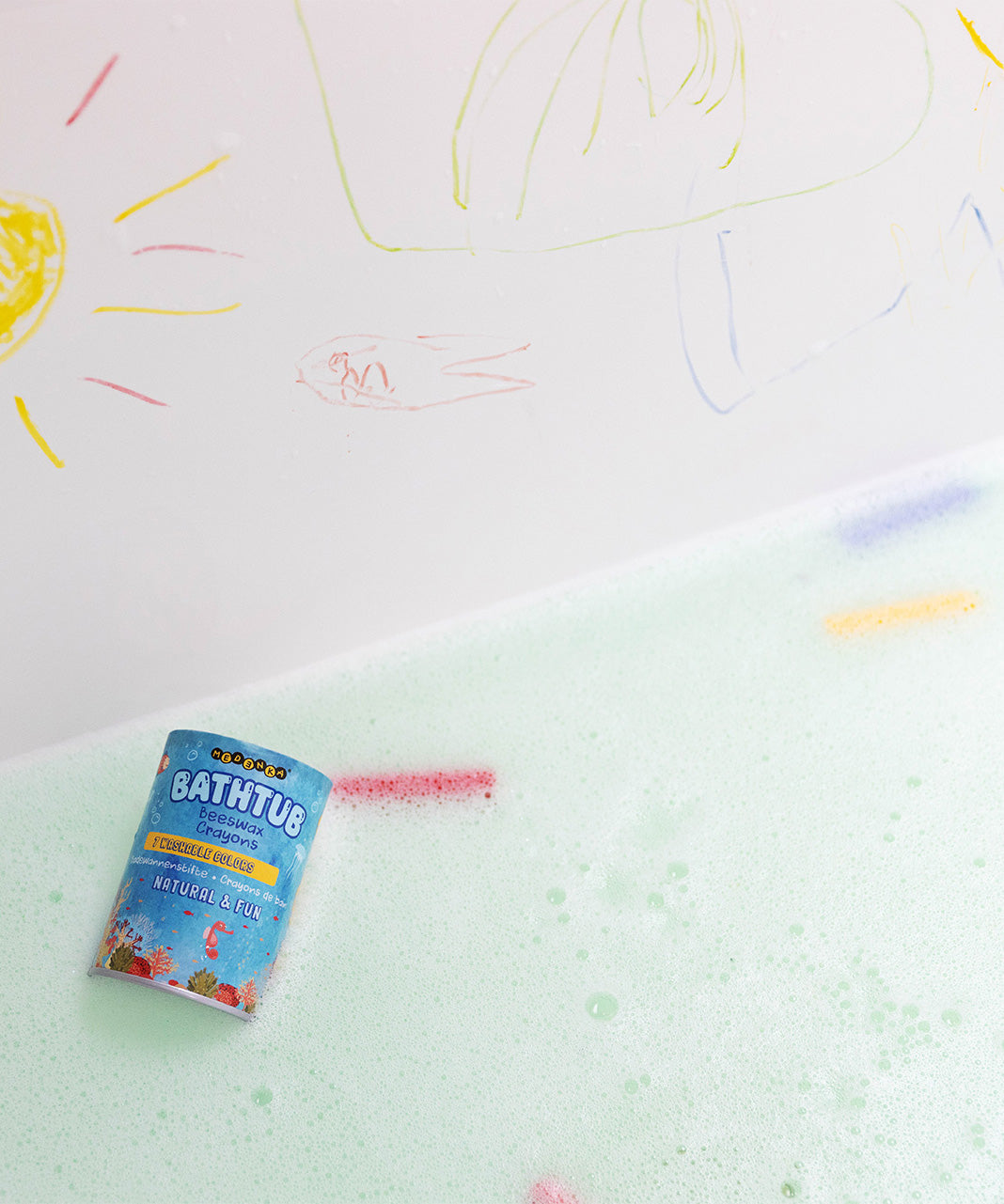 The Medenka beeswax bath crayons and their box floating in a bubbly bath tub.