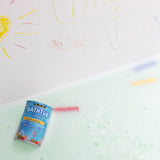 The Medenka beeswax bath crayons and their box floating in a bubbly bath tub.