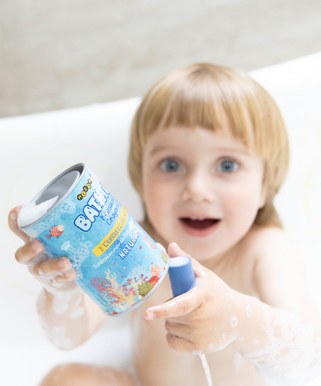 A child happily holding up a pack of Medenka beeswax bath crayons in the bath.