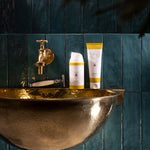 MÜHLE Organic Shaving Cream is stood on a golden sink next to the MÜHLE Organic Shaving Foam, on a dark blue tiled background